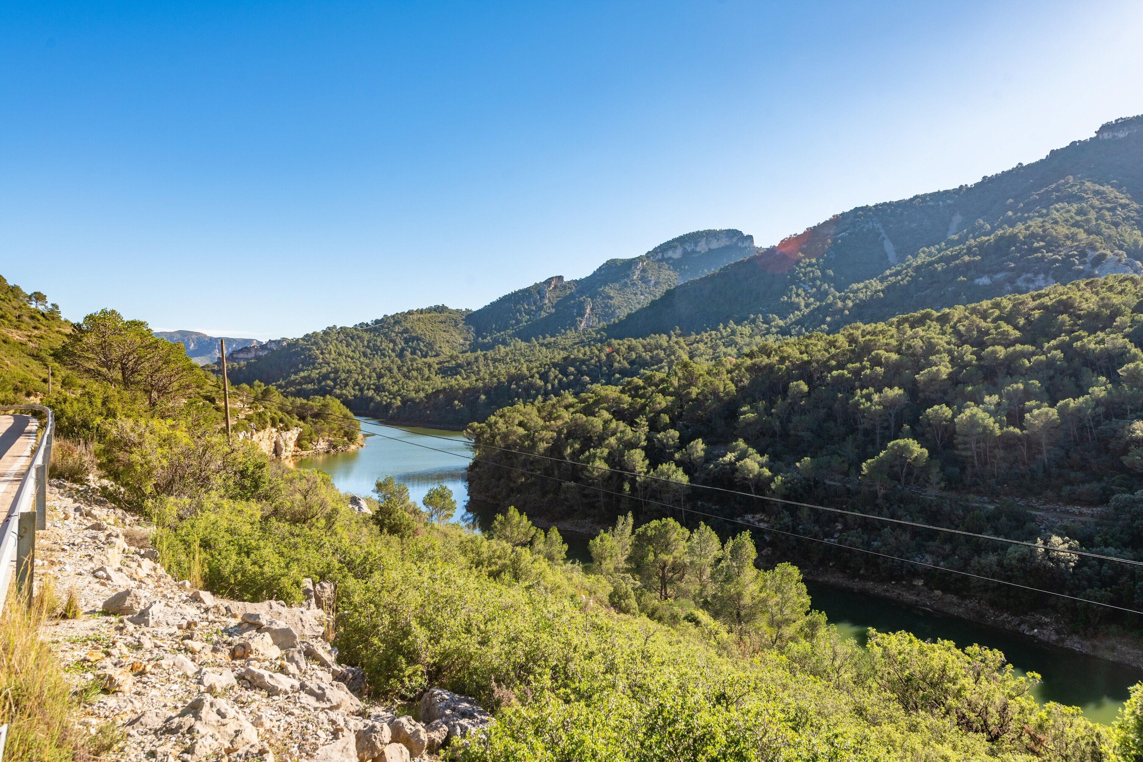 A mountainous landscape with a river, dense greenery, and a bridge.