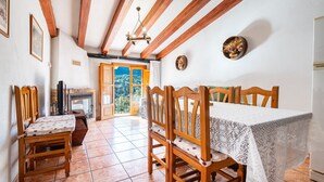 Un coin repas avec des chaises et une table en bois, une cheminée et une vue sur l’extérieur, visible à travers une porte.