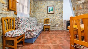 Una habitación con paredes de piedra, un sofá, dos sillas de madera, una chimenea y un cuadro enmarcado en la pared.