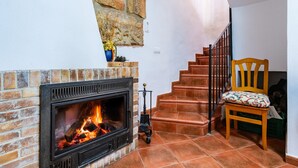 Una chimenea con pared de ladrillo, una silla de madera con cojín y una escalera con peldaños rojos.