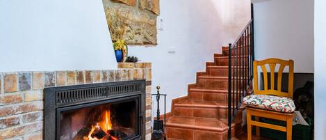 A fireplace with a brick wall, a wooden chair with a cushion, and a staircase with red steps.