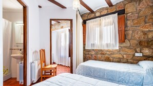 Un dormitorio con dos camas, una silla de madera, un radiador y una pared de piedra.