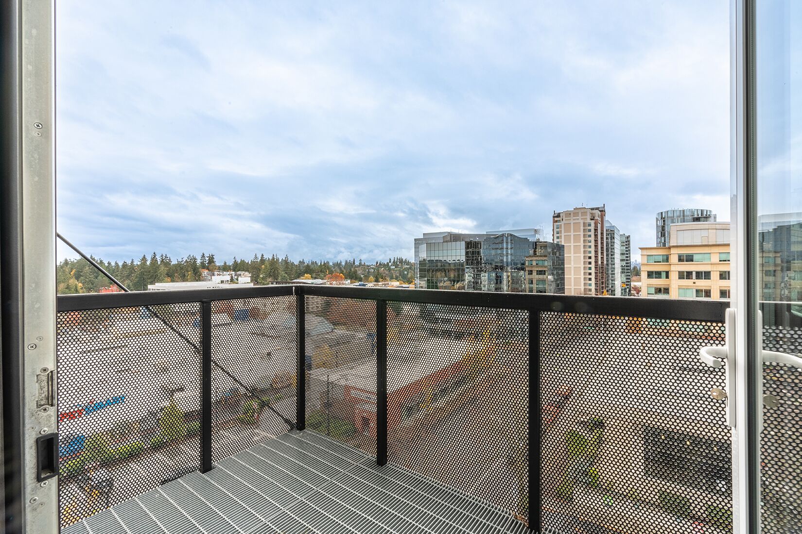 Un balcon doté d’une rambarde en métal, offrant une vue sur un paysage urbain avec des bâtiments et des arbres.