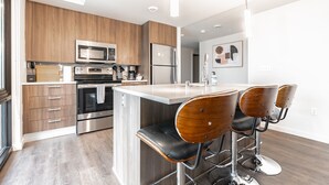 A modern kitchen with stainless steel appliances, wooden cabinets, and a central island with bar stools. - Sophari Downtown: Bellevue Apartments (Bellevue)