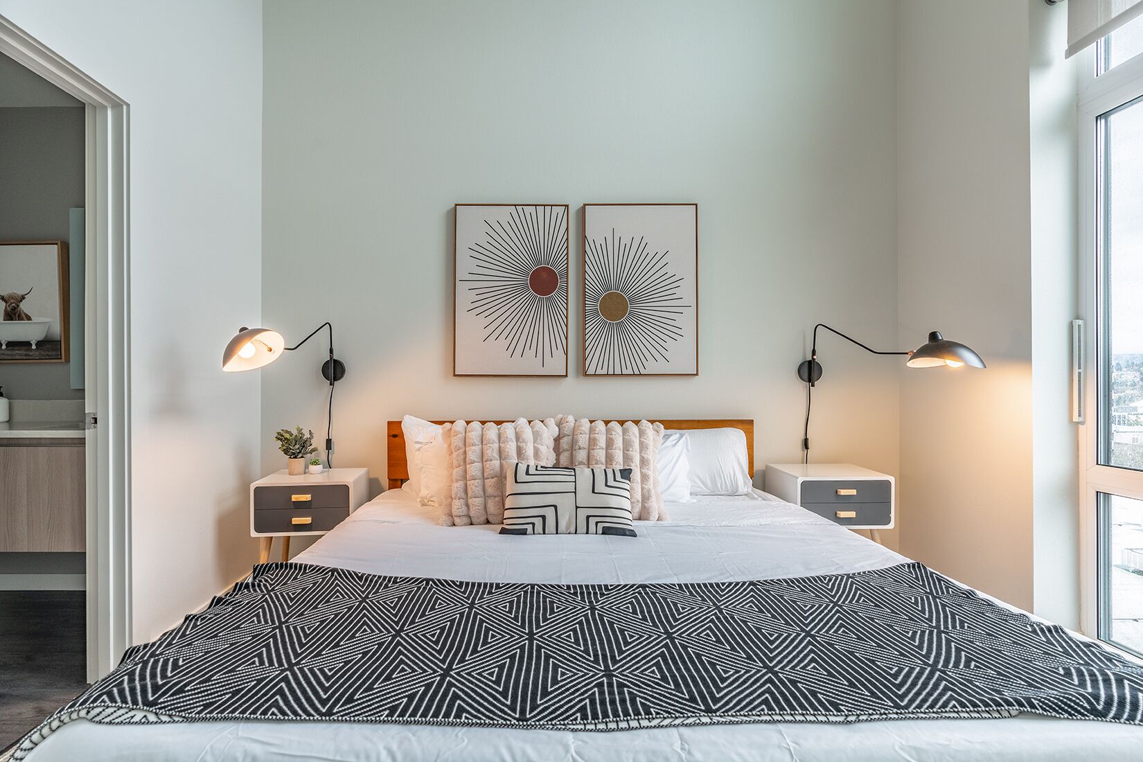 Ein modernes Schlafzimmer mit einem großen Bett, zwei Nachttischen, einer Kopfteil und zwei an der Wand befestigten abstrakten Kunstwerken.
