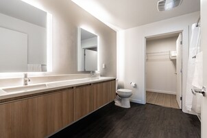 Un baño moderno con un espejo grande, armarios de madera, un inodoro y una ducha a ras de suelo.