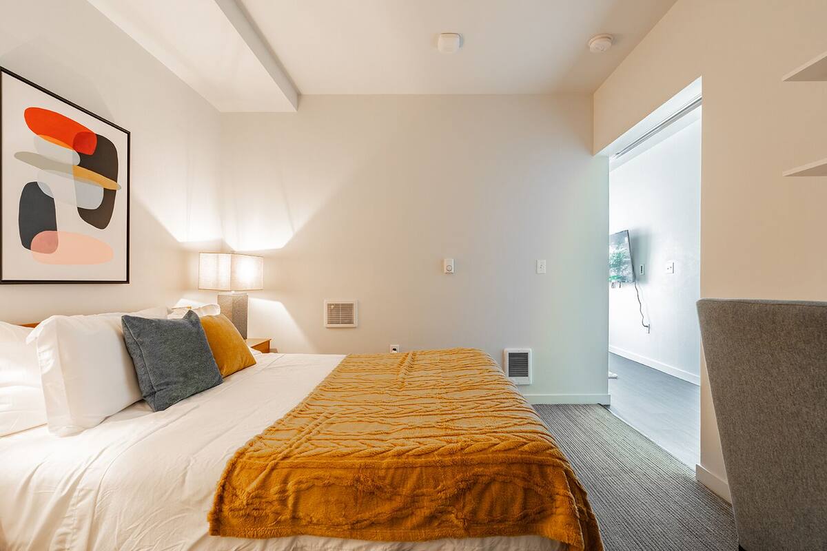 A hotel room with a bed, a large window, a flat-screen TV, and a painting on the wall.