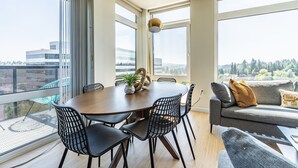 A modern living room with a round table, black chairs, a sofa, and a view of a cityscape through large windows. - Sophari Downtown: Bellevue Apartments (Bellevue)