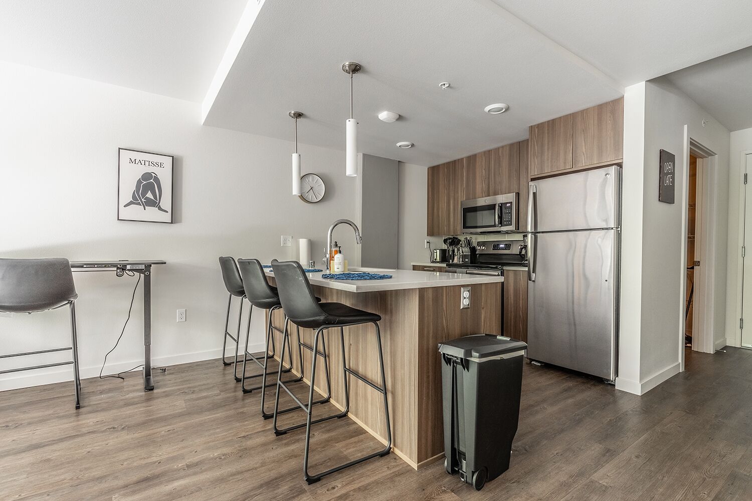 A modern kitchen with a central island, bar stools, a microwave, a refrigerator, and a trash bin.