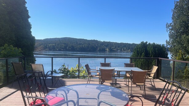 Une terrasse avec des sièges extérieurs donnant sur un lac, entourée d’arbres et de collines.