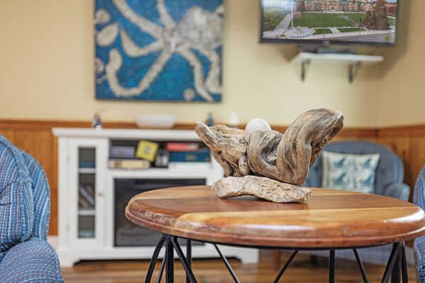 Une table basse en bois ornée d’un élément décoratif au centre, un téléviseur fixé au mur et une bibliothèque en arrière-plan.