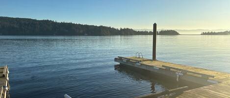 A wooden dock extending into calm water with a clear sky and forested hills in the background.