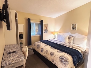 A bedroom with a bed, a desk, a chair, a wardrobe, and a window with curtains. - Oceanfront Cottage: Dock, Beach Access, Hot Tub, BBQ & Free Kayaks (Sooke)