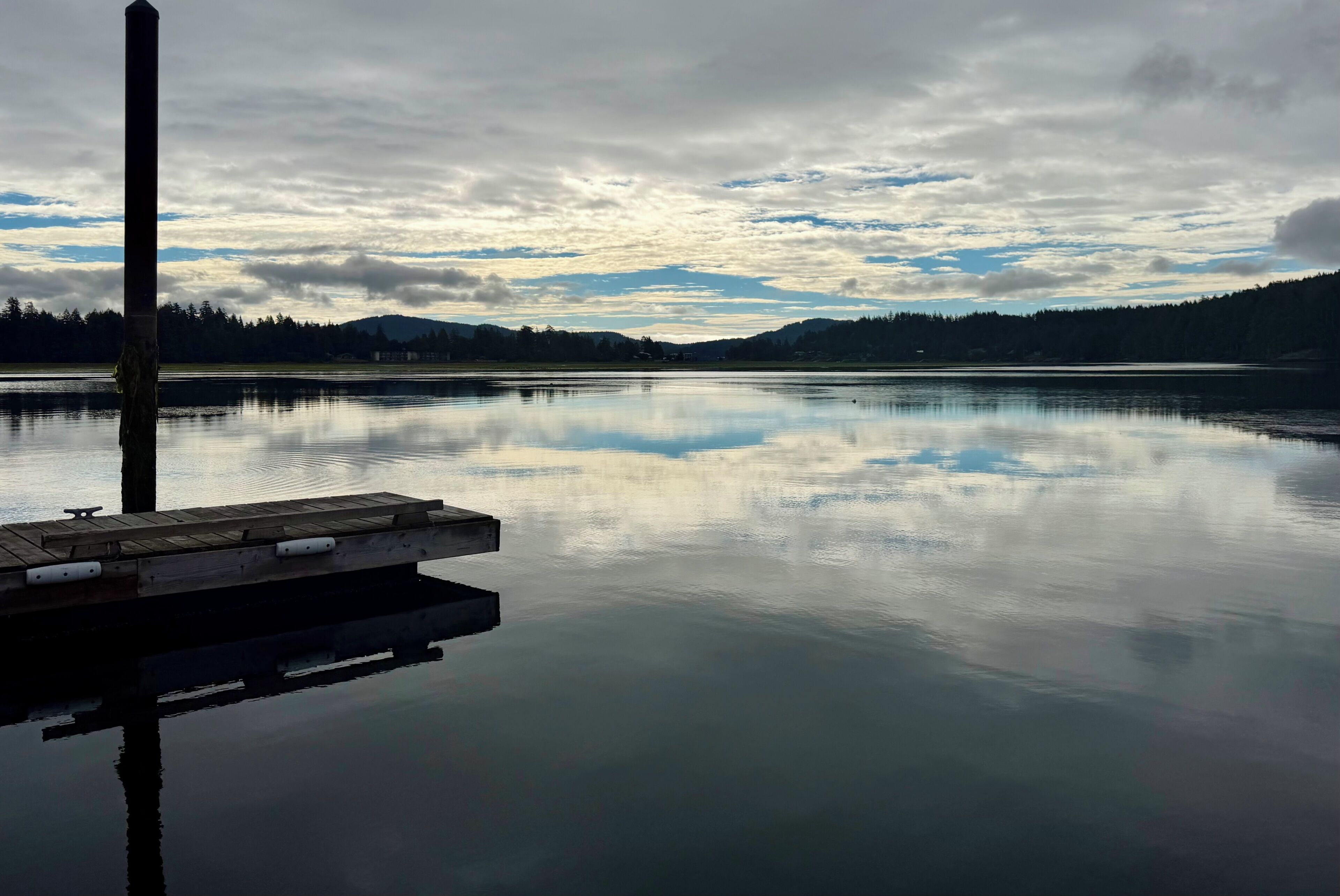 Un llac tranquil amb un moll que s'endinsa a l'aigua, envoltat d'un paisatge forestal i muntanyes allunyades.