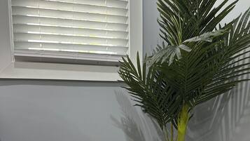 A corner of a room with a woven basket, a potted plant, and a window with blinds.