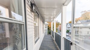 Ein überdachter Hauseingang mit Blick auf die Straße, ein Fenster mit Vorhang und eine Tür mit Griff.