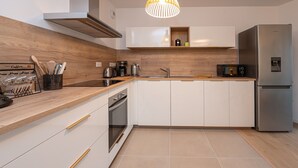 Una cocina moderna con armarios blancos, un refrigerador de acero inoxidable, encimera de madera y una lámpara colgante.