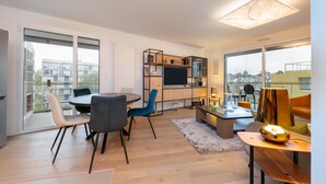 Una sala de estar moderna con comedor, cocina y ventanas amplias con vistas a la ciudad.
