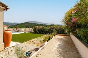 A courtyard with a pool, a large terracotta pot, and a view of hills.