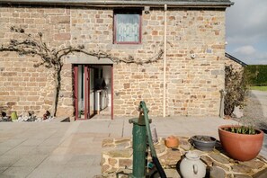 A stone building with a door, a window, a large potted plant, and a water pump.