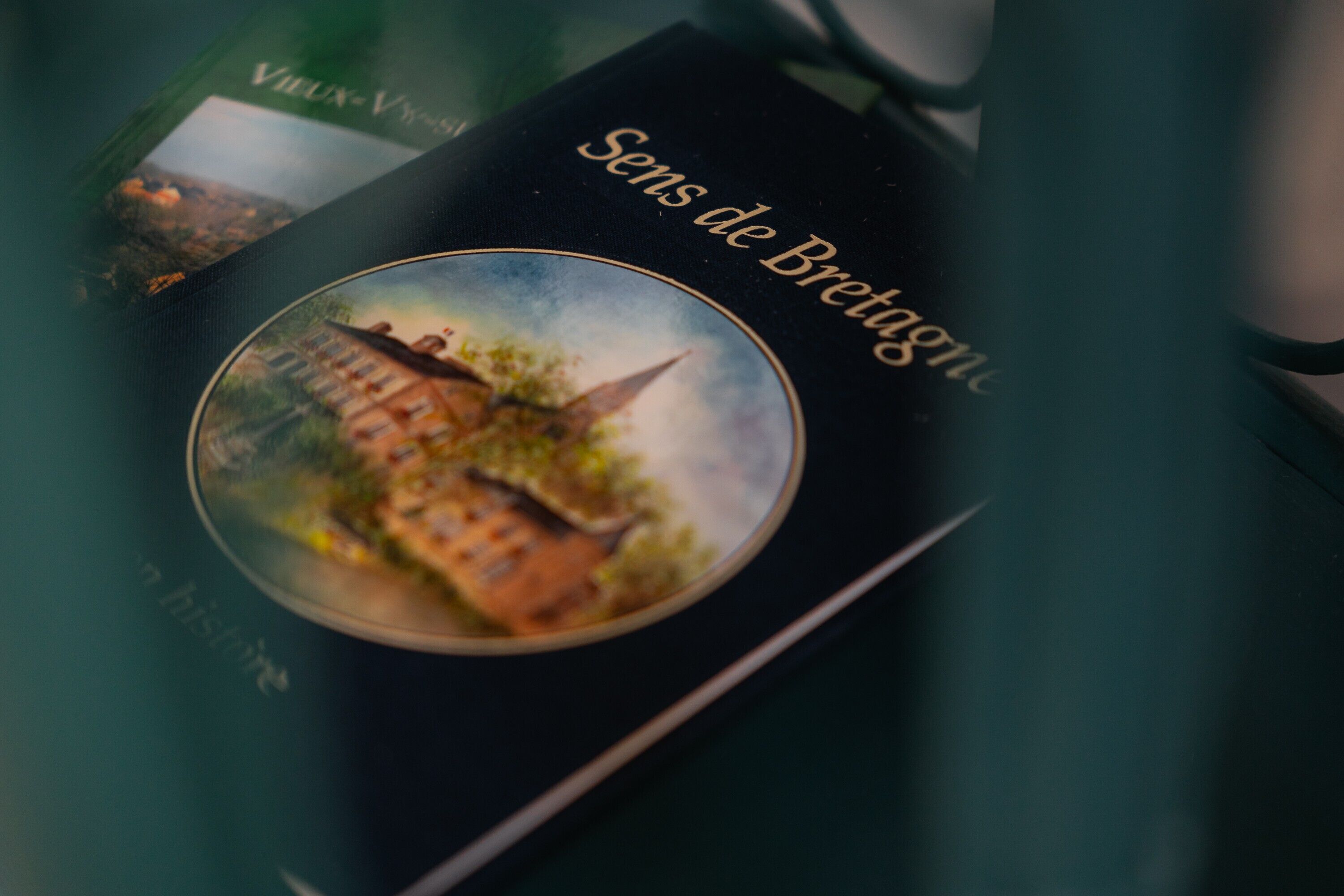 Een boek met de titel 'Sens de Bretagne', met een cirkelvormige afbeelding van een gebouw en een kerk op de omslag.
