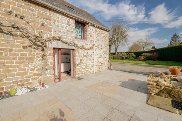 A stone building with a red door, a paved entrance, and a garden with potted plants.