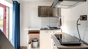 Una cocina compacta con estufa integrada, un lavamanos y una ventana con cortinas azules.