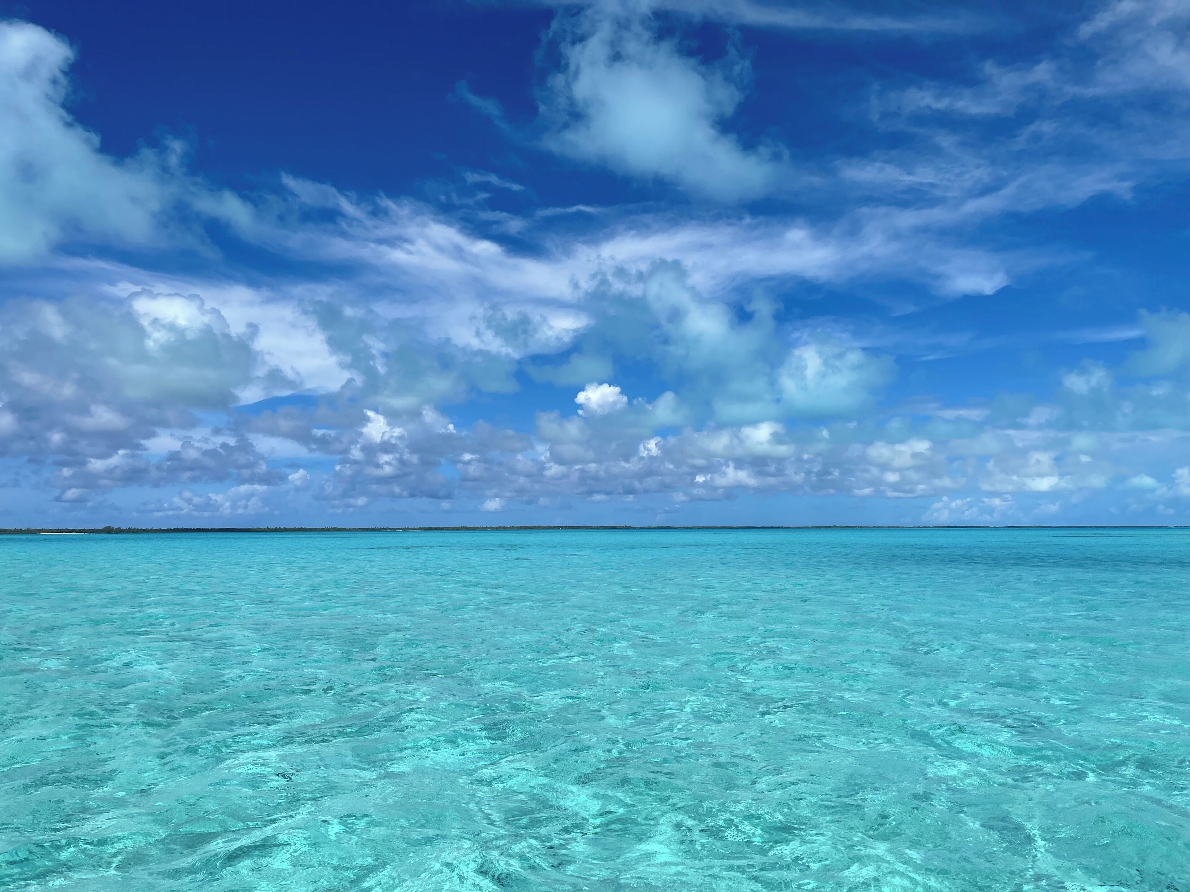 A clear view of turquoise ocean water and a blue sky with scattered clouds.