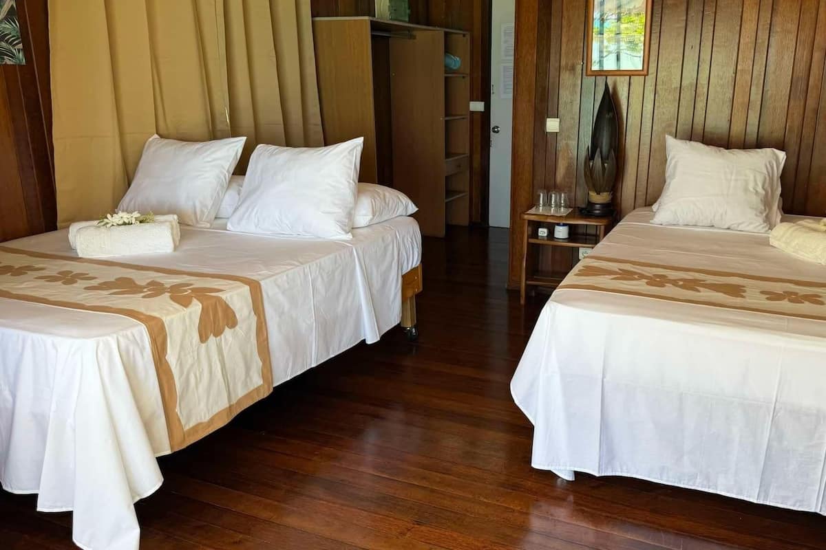 Dos camas dobles con sábanas blancas y estampados florales, piso de madera y cabecera de madera.