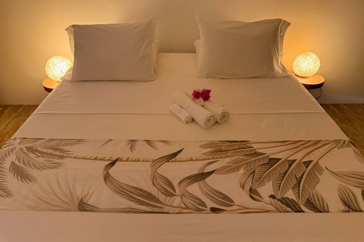 Una cama bien hecha con un edredón estampado con motivos florales, dos almohadas blancas y dos lámparas de noche.