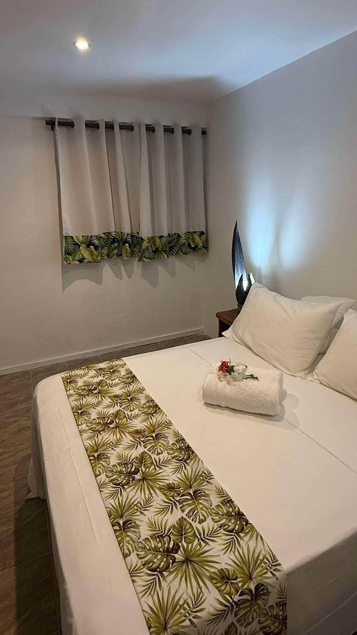 A neatly made bed with a floral-patterned bedspread, white pillows, and a neatly folded towel.