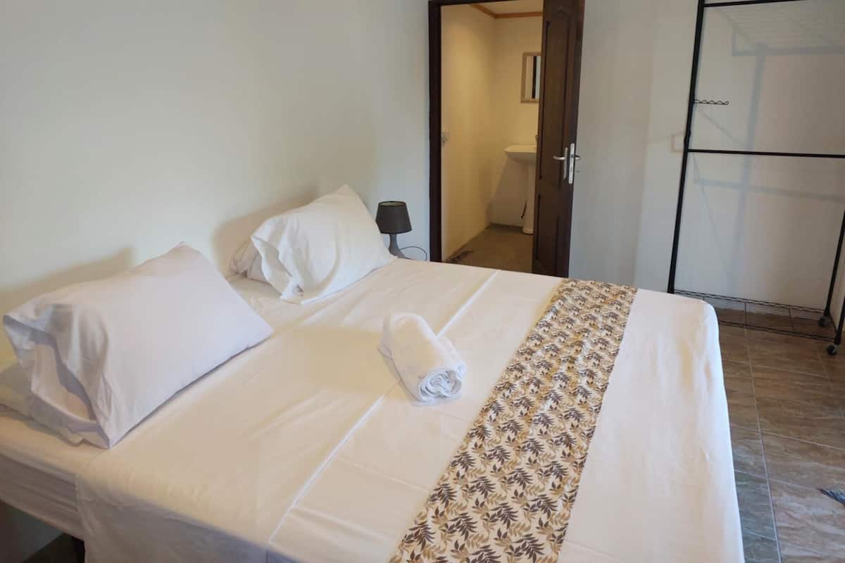 Una habitación de hotel con cama, mesita de noche, lámpara, puerta del baño y armario.