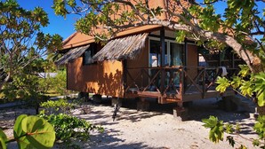 A rustic wooden house with a thatched roof, surrounded by lush greenery and a sandy ground. - Flyfishing Anaa Toku Kaiga (Anaa)