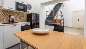 Una cocina compacta con microondas, pileta y alacenas, una mesa de comedor con un plato, y una escalera que lleva a otro nivel.