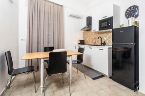 Une cuisine compacte comprenant une table à manger, des chaises, un réfrigérateur noir, un four à micro-ondes et une horloge murale.