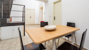 Un comedor con una mesa de madera, sillas negras, un cuenco blanco y una escalera, junto a una puerta blanca.