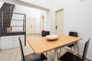 Un coin repas avec une table en bois, des chaises noires, un bol blanc, un escalier et une porte blanche.