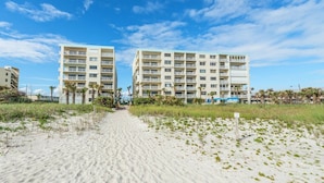 A pathway leading to two beachfront buildings with balconies, surrounded by sand and sparse vegetation. - Relax and Unwind Direct Ocean View with Heated Pool & Hot Tub (Cocoa Beach)