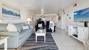 A spacious living room with a grey sofa, a coffee table, and a TV on a white cabinet. - Relax and Unwind Direct Ocean View with Heated Pool & Hot Tub (Cocoa Beach)