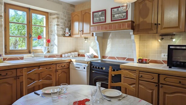 Une cuisine avec des meubles de rangement en bois, une cuisinière, un évier et une table à manger mise avec des verres et des assiettes.