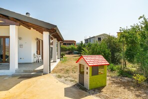 Una propiedad residencial con un porche cubierto, una casita de juegos y un jardín.