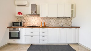 Et køkken med hvide skabe, en mikrobølgeovn, ovn, gasblus og et flisebeklædt backsplash.