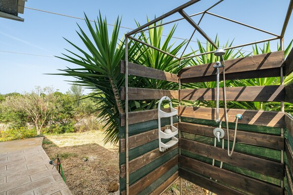 Una pérgola de madera con un rociador de ducha y un estante blanco.