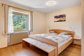 Une chambre avec un lit en bois, une fenêtre avec des rideaux, un radiateur et un tableau accroché au mur.