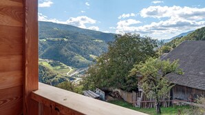 A wooden balcony overlooking a valley with a mountain, a tree, and a rustic building. - Room 'Oberhemberger Hof Dreier' with Mountain View, Shared Terrace and Wi-Fi (Feldthurns)