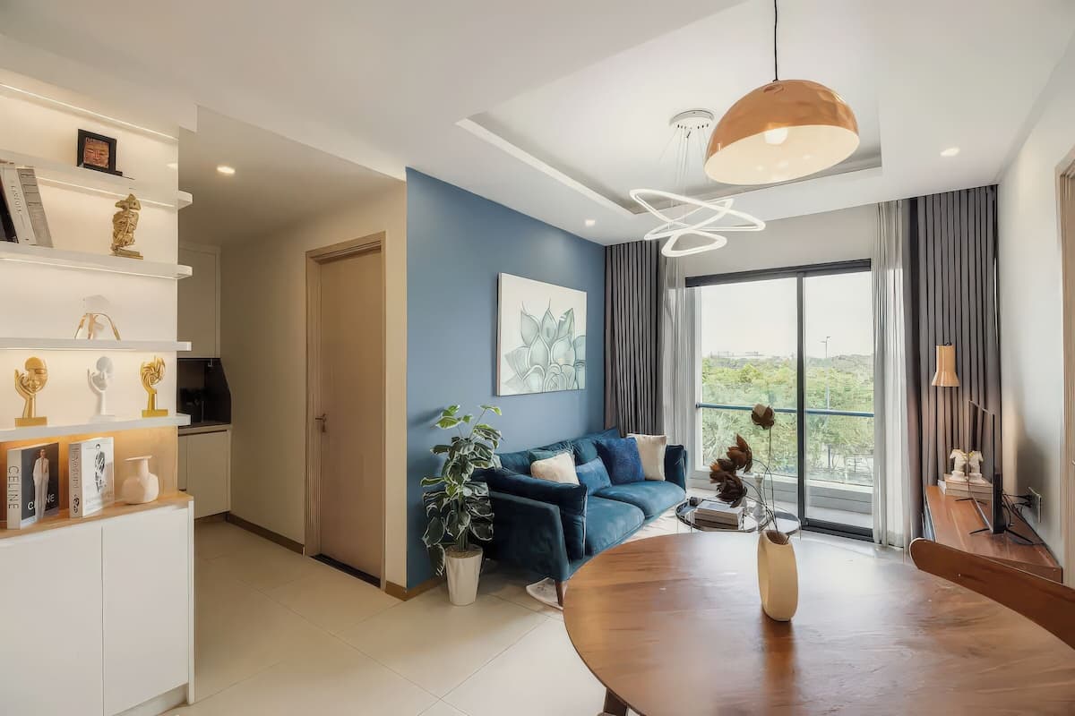A modern living room with a blue accent wall, a large window, a dining table, and a sofa.