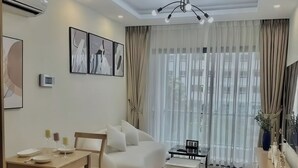 A modern living room with a sofa, dining table, and a coffee table. There are curtains, a ceiling light, and artwork on the wall. - New City Thu Thiem D2 (Ho Chi Minh City)
