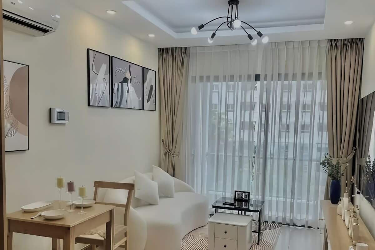 A modern living room with a sofa, dining table, and a coffee table. There are curtains, a ceiling light, and artwork on the wall.