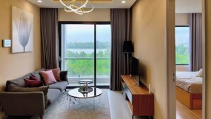 A modern hotel room with a sofa, a round coffee table, a TV, and a balcony with a view of the city. - New City Thu Thiem D2 (Ho Chi Minh City)