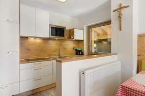 Una cucina con piano di lavoro in legno, mobili bianchi, un forno a microonde, una macchina da caffè e una finestra con cornice in legno.